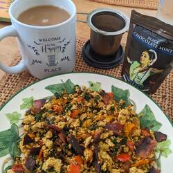 A plate of tofu veggie scramble with a mug of tea, an infuser, and a bag of chocolate mint loose leaf black tea in the background.