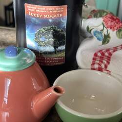 A large tin of Lucky Summer Rooibos behind a colorful teapot and teacup set.