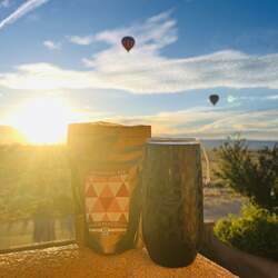 A bag of Pumpkin tea next to a black tea tumbler with a sunrise and floating hot air balloons in the background.