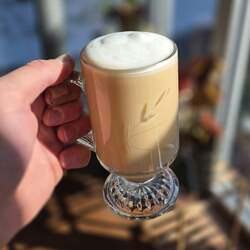 A glass mug of rooibos earl grey london fog with a bit of foamy milk on top, held in front of a window.