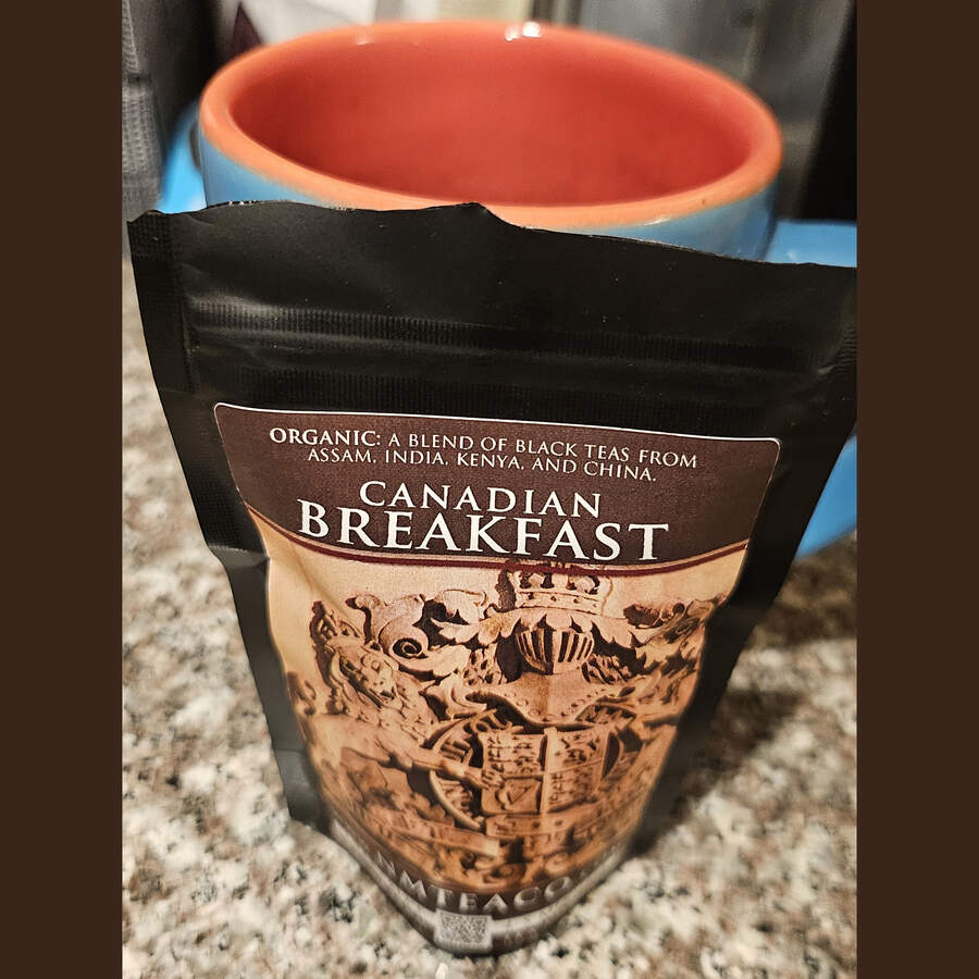 A close up on a bag of Canadian Breakfast black tea with just the top of a blue and orange mug peeking out from behind it.