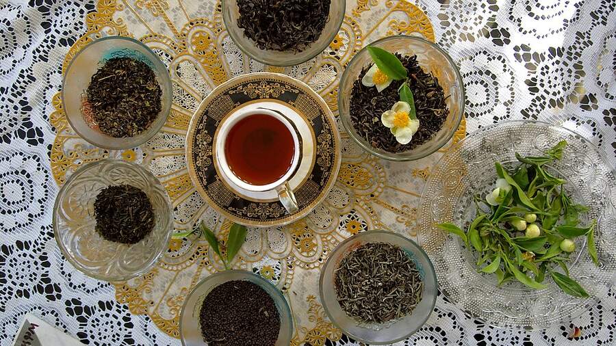 A cup of black tea, surrounded by different types of black tea leaves
