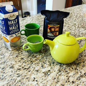 A bag of Cream Earl Grey tea pictured with a lime green teapot, two green cups, and a carton of half and half.