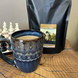 A mug full of chai latte made with the masala spice mix in the background, and a chess board pictured to the far left of the picture and behind the mug.