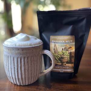 A bag of Honeybush Banana Nut tea next to a mug full of brewed tea with latte foam on top