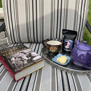 A hardcover book next to a silver tray with a purple teapot, a small plate of shortbread cookies, a black tea cup, and a bag of Vintage Earl Grey tea on it.