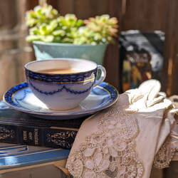 A vintage tea cup filled with Scottish Breakfast black tea on top of a vintage copy of Pride and Prejudice and a vintage pair of white lace gloves.